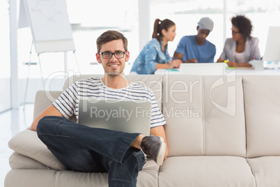 Man using laptop with colleagues in background at creative offic