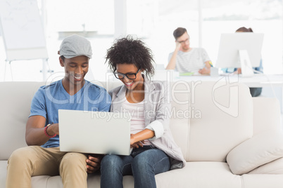 Couple using laptop with colleagues in background at creative of