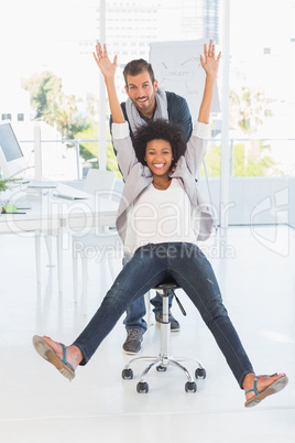 Playful young man pushing woman on chair in office