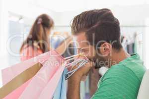 Bored man with shopping bags while woman by clothes rack