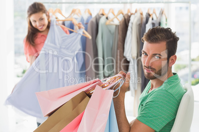 Bored man with shopping bags while woman by clothes rack