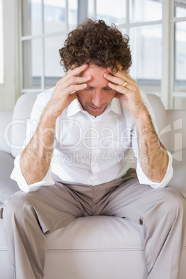Worried well dressed man sitting with head in hands on sofa in t