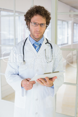 Serious male doctor standing with clipboard in hospital Serious male doctor standing with clipboard in hospital
