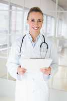 Happy beautiful female doctor with clipboard in hospital