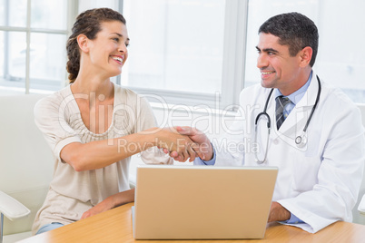 Doctor and patient shaking hands by laptop in office