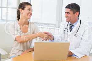 Doctor and patient shaking hands by laptop in office