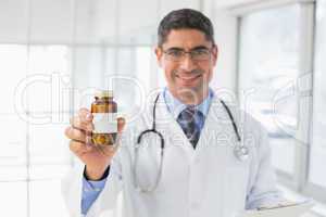 Smiling male doctor with a bottle of pills in hospital