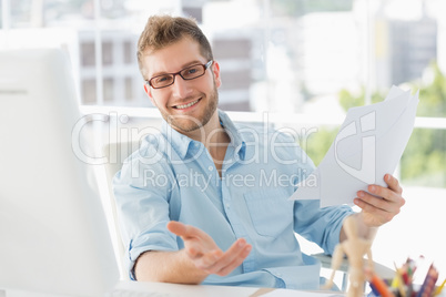 Happy designer sitting at his desk gesturing at camera