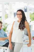 Brunette designer smiling at camera leaning on desk