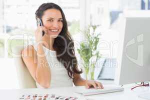 Beautiful editor talking on phone at her desk smiling at camera
