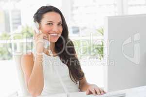 Beautiful businesswoman on telephone at her desk smiling at came