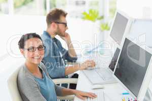 Team of young designers working at desk with woman smiling at ca