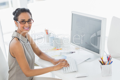 Designer working at her desk using computer smiling at camera
