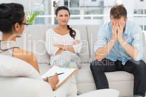 Unhappy couple sitting on sofa at therapy session