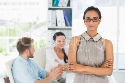 Attractive woman smiling at camera while colleagues chat at desk