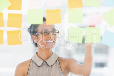 Young smiling designer looking at sticky notes on window