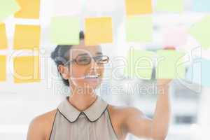 Young smiling designer looking at sticky notes on window