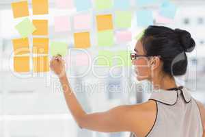 Smiling designer looking at sticky notes on window