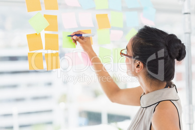 Smiling designer writing on sticky notes on window