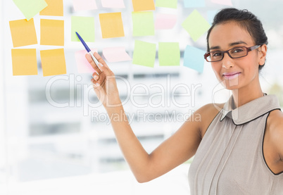 Designer pointing to sticky notes on window smiling at camera