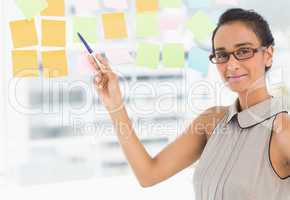 Designer pointing to sticky notes on window smiling at camera