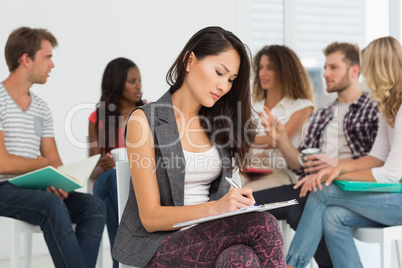 Woman taking notes while colleagues are talking behind her