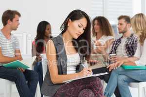 Woman taking notes while colleagues are talking behind her