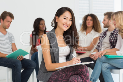 Smiling woman taking notes while colleagues are talking behind h