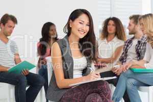Smiling woman taking notes while colleagues are talking behind h