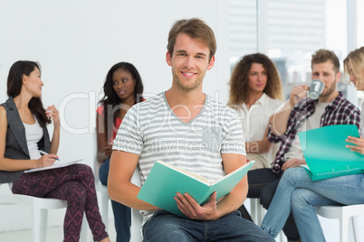 Smiling man taking notes while colleagues are talking behind him