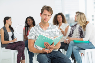 Happy man holding notebook while colleagues are talking behind h