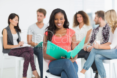 Smiling woman holding notebook while colleagues are talking behi