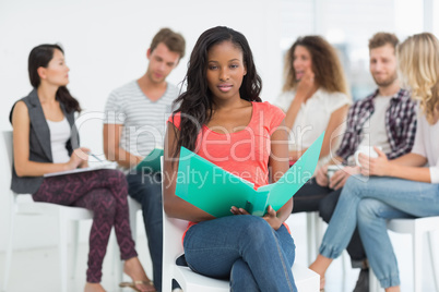 Happy woman holding notebook while colleagues are talking behind