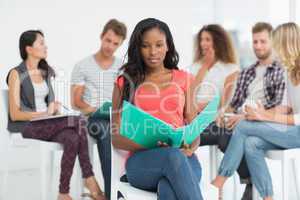 Happy woman holding notebook while colleagues are talking behind