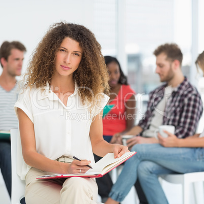 Focused woman writing while colleagues are talking behind her