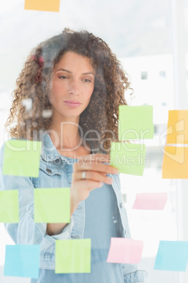 Focused pretty designer looking at sticky notes on window