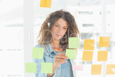 Smiling pretty designer looking at sticky notes on window