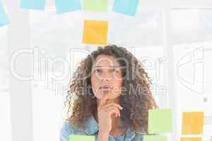 Thoughtful pretty designer looking at sticky notes on window