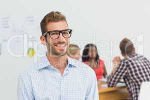 Handsome designer smiling at camera with colleagues behind him