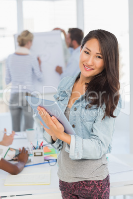 Asian woman using her tablet while her colleagues are working