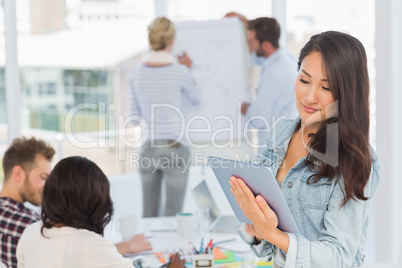 Asian woman using her tablet pc while her colleagues are working