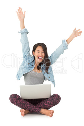 Asian woman cheering at camera with laptop sitting on floor