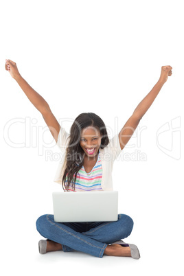Pretty young woman cheering at camera with laptop sitting on flo