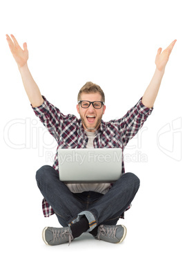 Handsome man cheering at camera with laptop sitting on floor