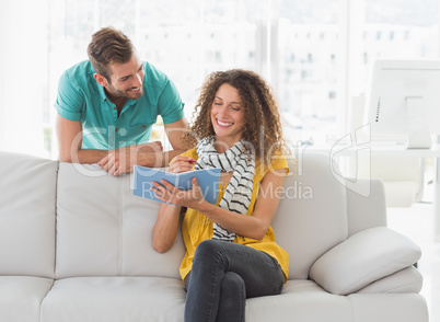 Smiling woman on the couch showing her colleague her notebook