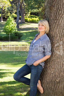 Woman leaning on tree trunk in park