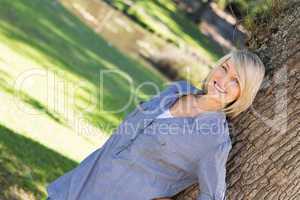 Woman leaning on tree trunk in parkland