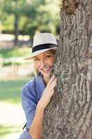 Smiling woman hiding behind tree trunk