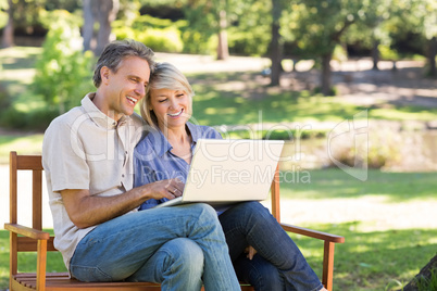 Couple using laptop on park bench