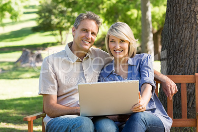 Happy couple using laptop in park